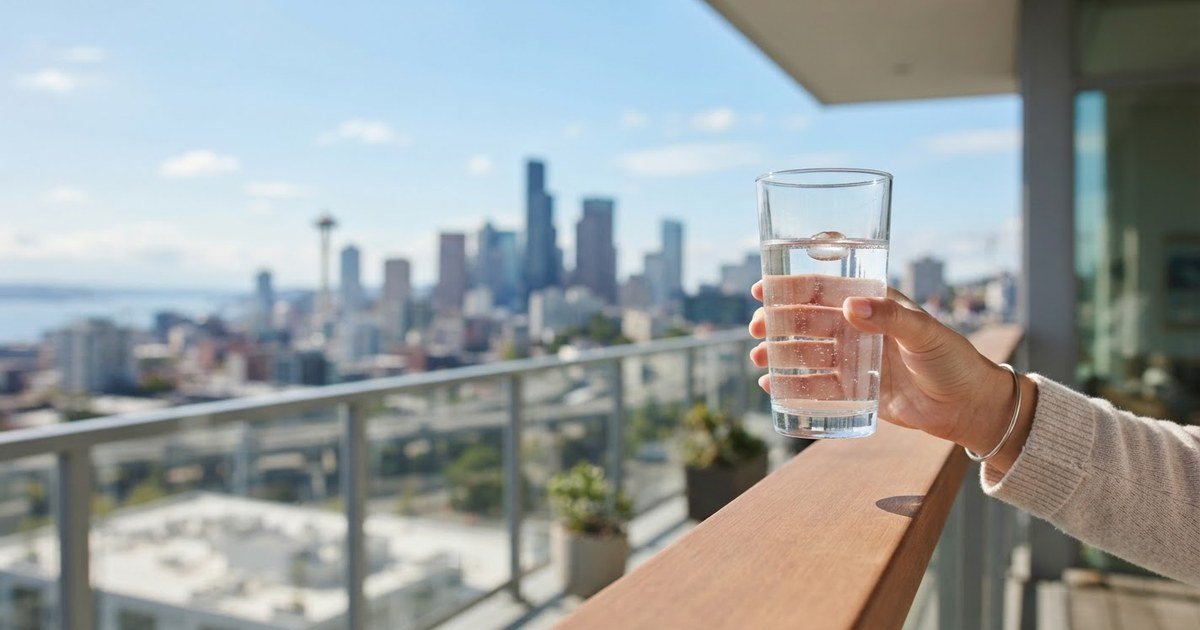 Hand holding a crystal-clear glass of tap water in front of a sunny American city skyline